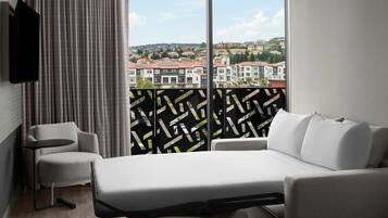 A hotel room with a bed, a sofa, a TV, and a view of a residential area.