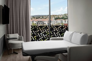 Habitación de hotel con cama, sofá, televisión y vistas a una zona residencial.