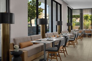 Un restaurante moderno con una barra alargada, asientos acolchados y grandes ventanales.