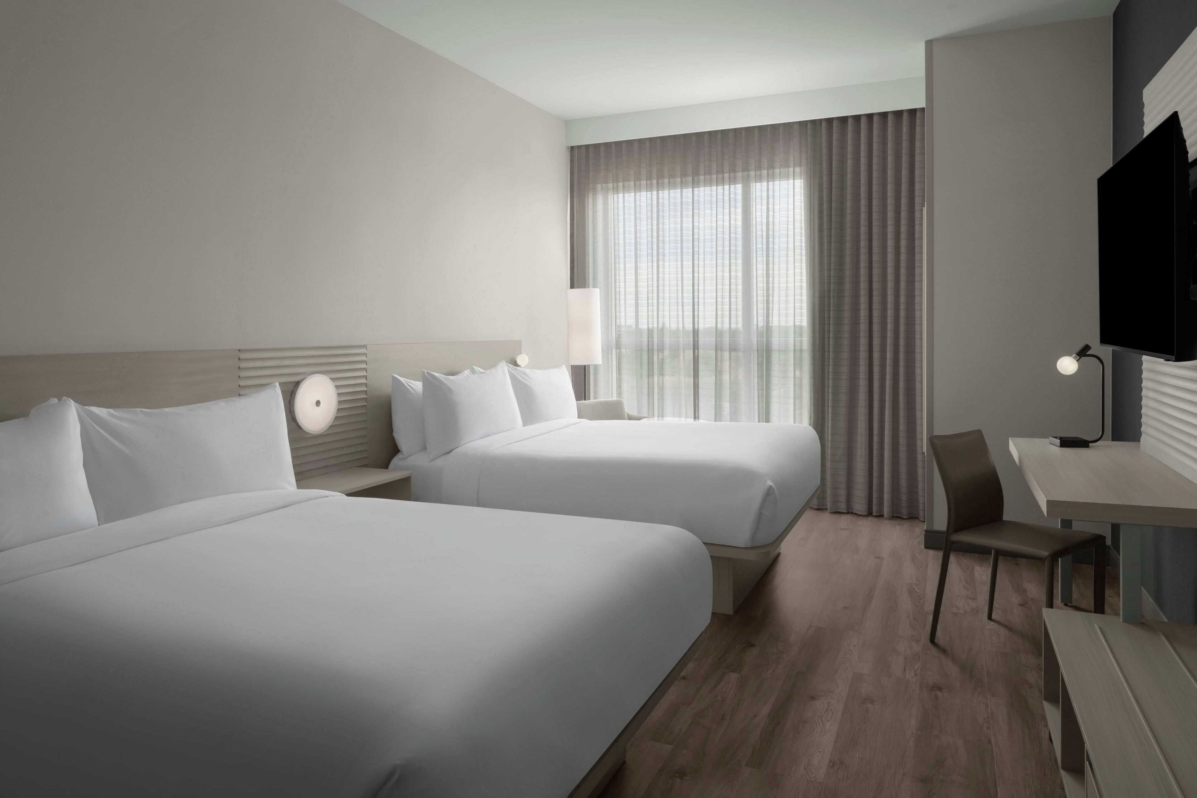 A hotel room with two beds, a desk, a chair, a TV, and a window with curtains.