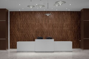 A reception area with a wooden panel wall, a white reception desk, and pendant lighting. - AC Hotels by Marriott Sacramento Folsom (Folsom)