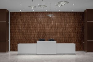 Un área de recepción con un panel de madera en la pared, un mostrador blanco y luminarias colgantes.