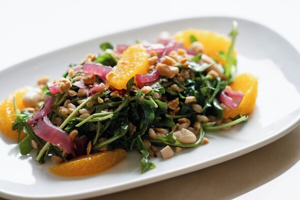 A plate of food with greens, nuts, and orange slices.