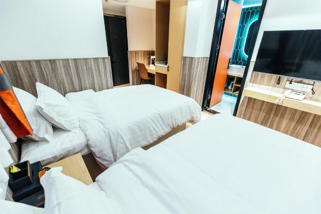Hotelkamer met twee bedden, een bureau, een stoel, een televisie en een badkamer met spiegel en wastafel.