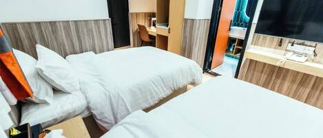 A hotel room with two beds, a desk, a chair, a TV, and a bathroom with a mirror and sink.