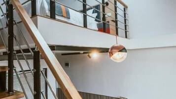 Un intérieur moderne avec un escalier en bois, une mezzanine comprenant un lit, un bureau avec une chaise et un luminaire suspendu.