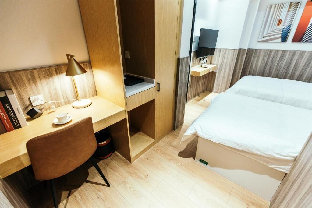 Quarto de hotel com escrivaninha, cadeira, cama e espelho.