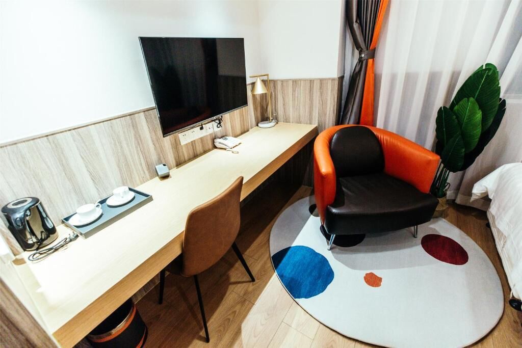 Habitación de hotel con escritorio, silla, televisor y una planta.