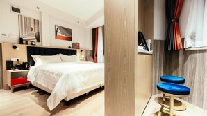 Ein modernes Hotelzimmer mit Bett, Nachttisch und einem kleinen Hocker.
