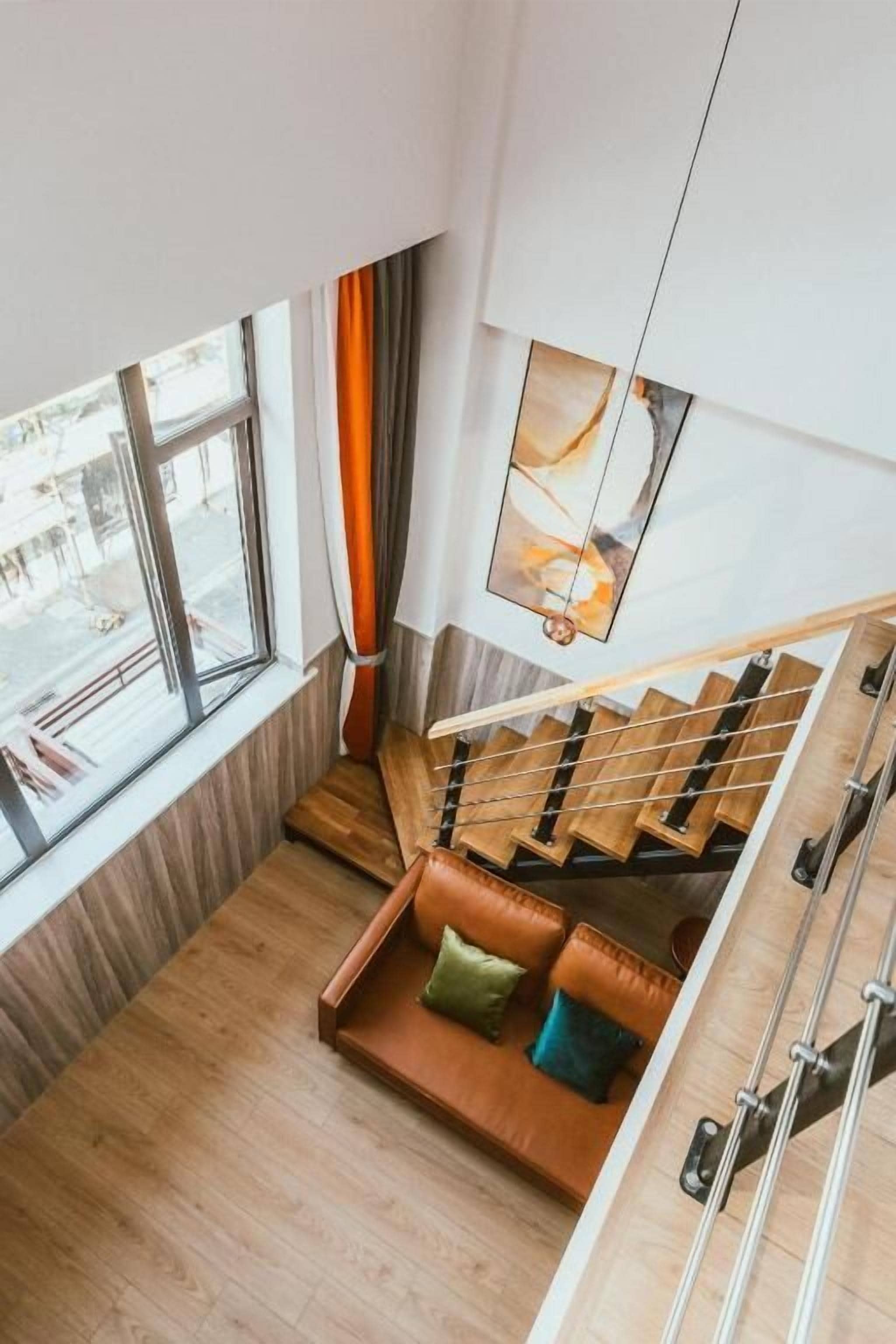 Un interior moderno con una escalera de madera, una zona de estar con cojines y un ventanal que ofrece vistas al exterior.