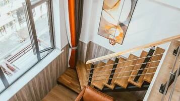 Un interior moderno con una escalera de madera, una zona de estar con cojines y un ventanal que ofrece vistas al exterior.