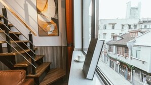 Eine Treppe mit Holzboden und Metallgeländern, ein brauner Ledersessel, ein gerahmtes Bild an der Wand und ein Fenster mit Blick auf die Stadt.