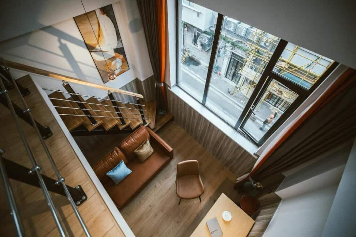 Een modern interieur met een trap, een bruine leren bank, een houten tafel en een groot raam met uitzicht op de straat.