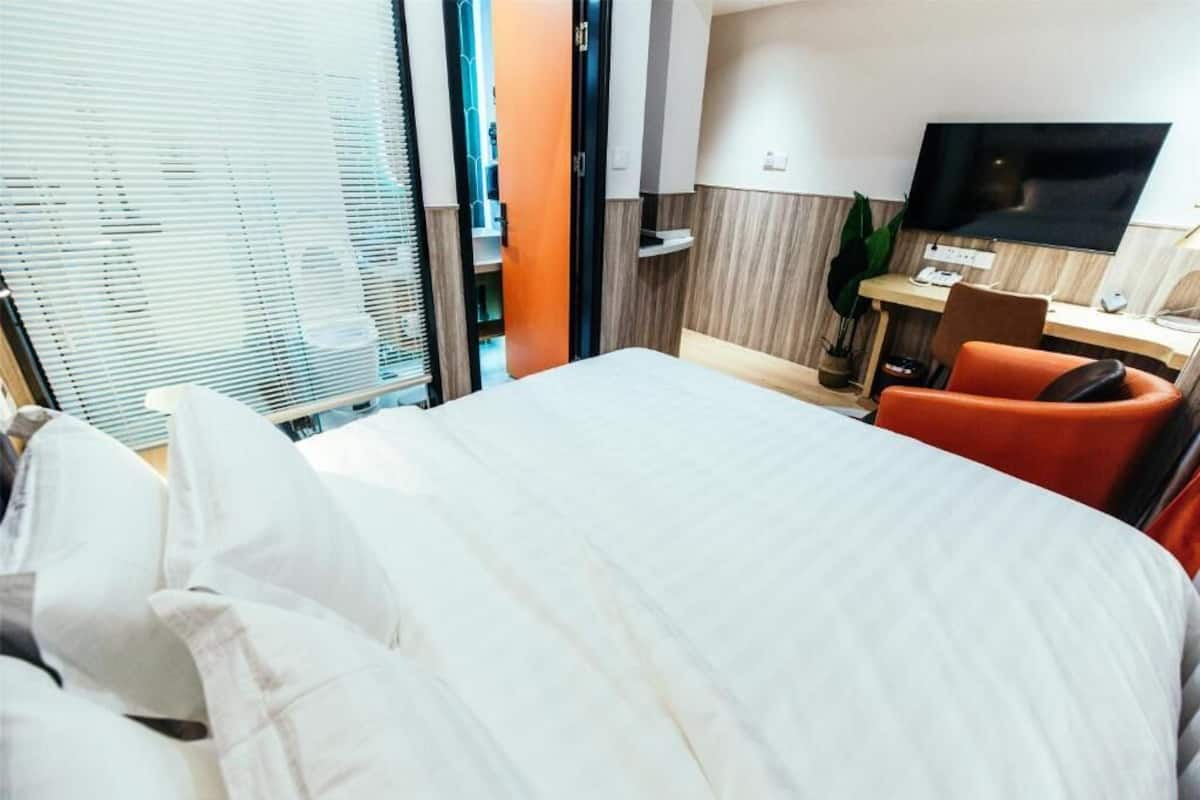 Een hotelkamer met een bed, een bureau met stoel, een televisie en een raam met zonwering.