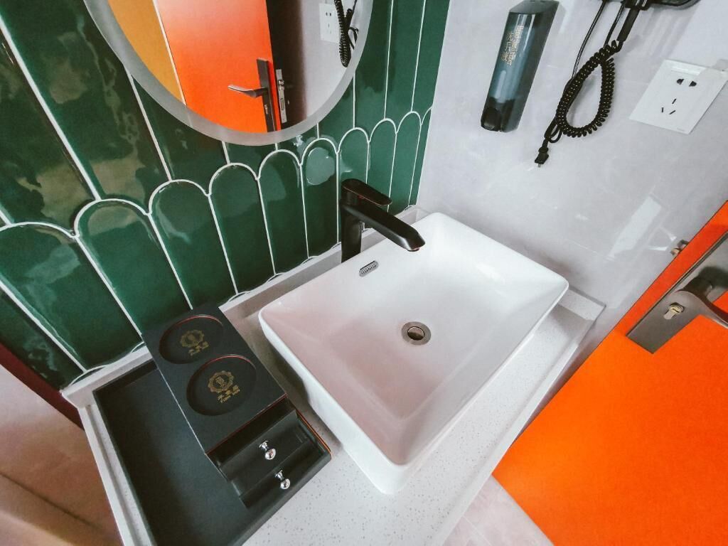 Un bagno con un lavandino bianco, uno specchio e una parete rivestita di piastrelle verdi.