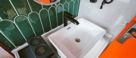 Un bagno con un lavandino bianco, uno specchio e una parete rivestita di piastrelle verdi.