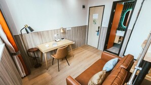 Ein gemütlicher Raum mit Holzboden, einer braunen Ledersofa, einem kleinen Schreibtisch mit Stuhl und einer Lampe.