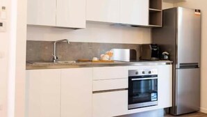 Eine kompakte Küche mit weißen Schränken, einem Edelstahlkühlschrank, einem eingebauten Backofen und einer Arbeitsplatte mit einer Kaffeemaschine.