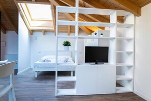 A modern room with a skylight, a bed, a TV, and a white shelving unit.