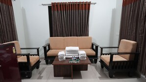 Een kamer met een bank, twee fauteuils, een bijzettafeltje met handdoeken en toiletartikelen, en een koelkast.