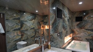 Een moderne badkamer met marmeren wanden, een grote spiegel, een dubbele wastafel, een toilet en een bad.