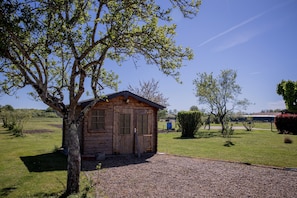 Une cabane en bois avec une allée en gravier, entourée d’un champ herbeux et d’arbres.