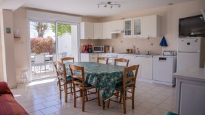 Una cocina con una mesa de comedor, sillas, microondas, refrigerador y puerta corrediza de vidrio que da a un espacio exterior.