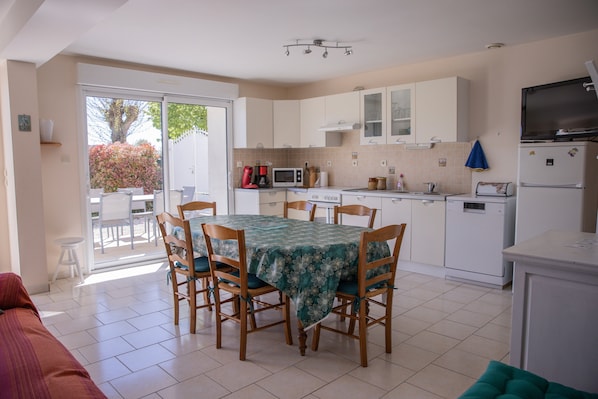 Une cuisine équipée d’une table à manger, de chaises, d’un four à micro-ondes, d’un réfrigérateur et d’une porte-fenêtre coulissante donnant sur un espace extérieur.