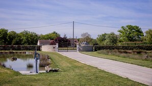 Un camino de entrada con puerta pasa a una casa con un estanque bajo un cielo despejado.