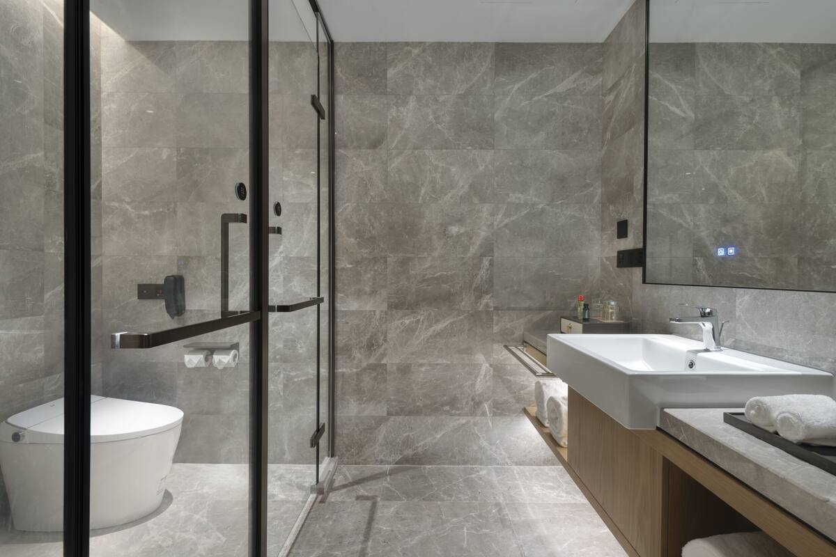 A modern bathroom with a glass shower enclosure, a white toilet, a large sink with a mirror, and a wooden vanity.