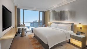 Ein modernes Hotelzimmer mit einem großen Bett, einem Schreibtisch, einem Fernseher und Blick auf die Stadt.