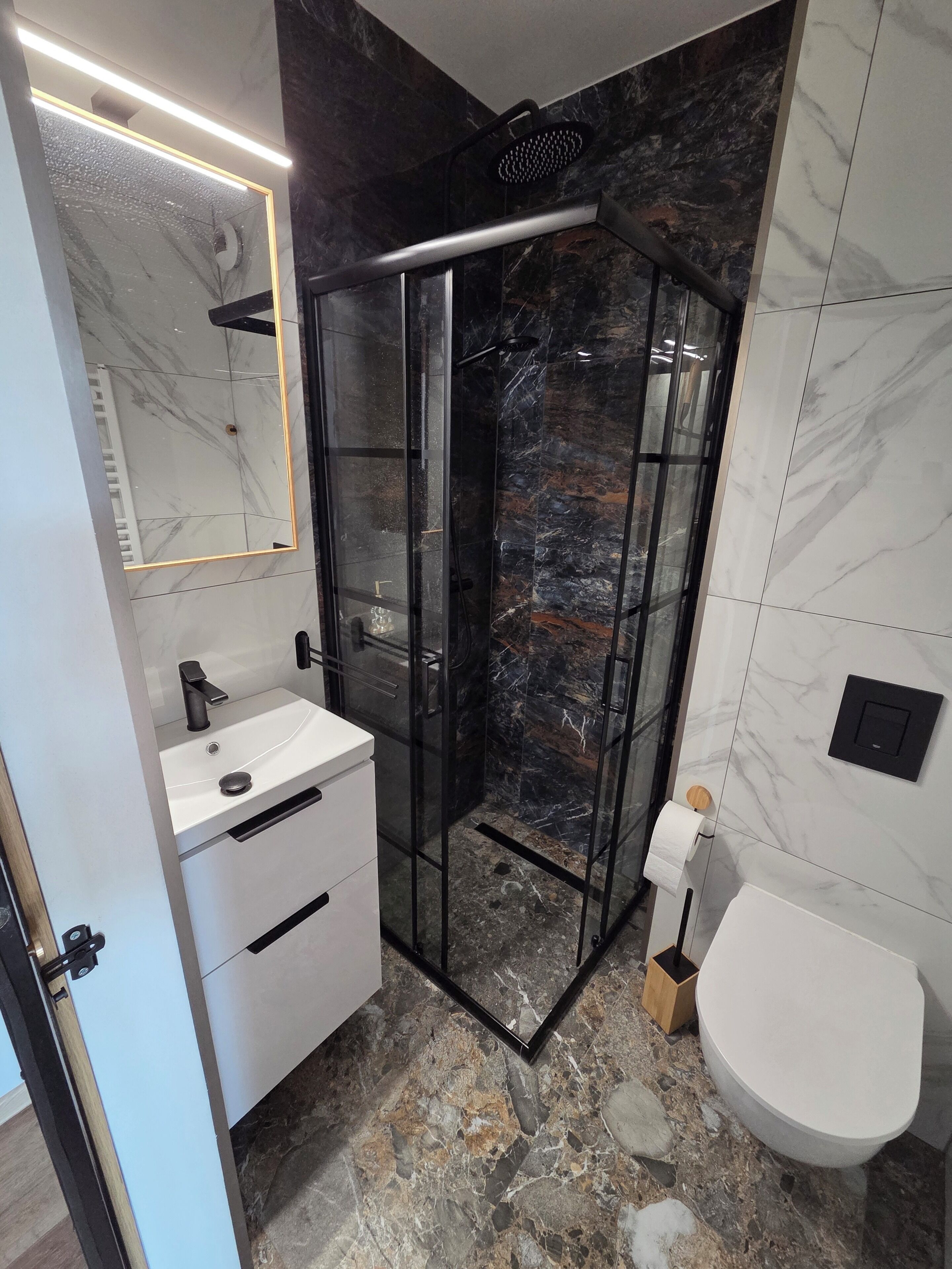 Ein modernes Badezimmer mit einer Duschkabine, einem weißen Waschbecken und einer Toilette.