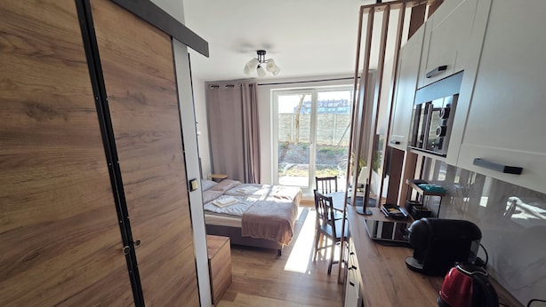 A modern bedroom with a wooden wardrobe, a bed with a headboard, a desk with a chair, and a view of the outdoors. - Modern studio near Krakow Old Town + WiFi (Kraków)