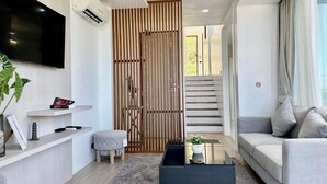 Una sala de estar moderna con un televisor de pantalla plana, un sofá, una mesa de centro y una escalera que sube a un nivel superior.