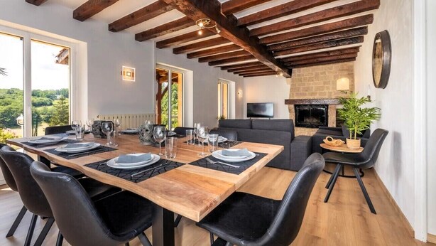 A dining area with a wooden table, black chairs, and a stone fireplace. - Villa Dorlot (Cazals)