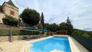 A swimming pool with a curved edge, surrounded by a stone deck and a few lounge chairs. - Villa Dorlot (Cazals)