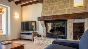 A living room with a stone fireplace, a flat-screen TV, a sofa, and a wooden coffee table. - Villa Dorlot (Cazals)