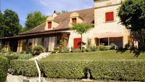 A stone building with red shutters, a tiled roof, and a well-maintained garden. - Villa Dorlot (Cazals)