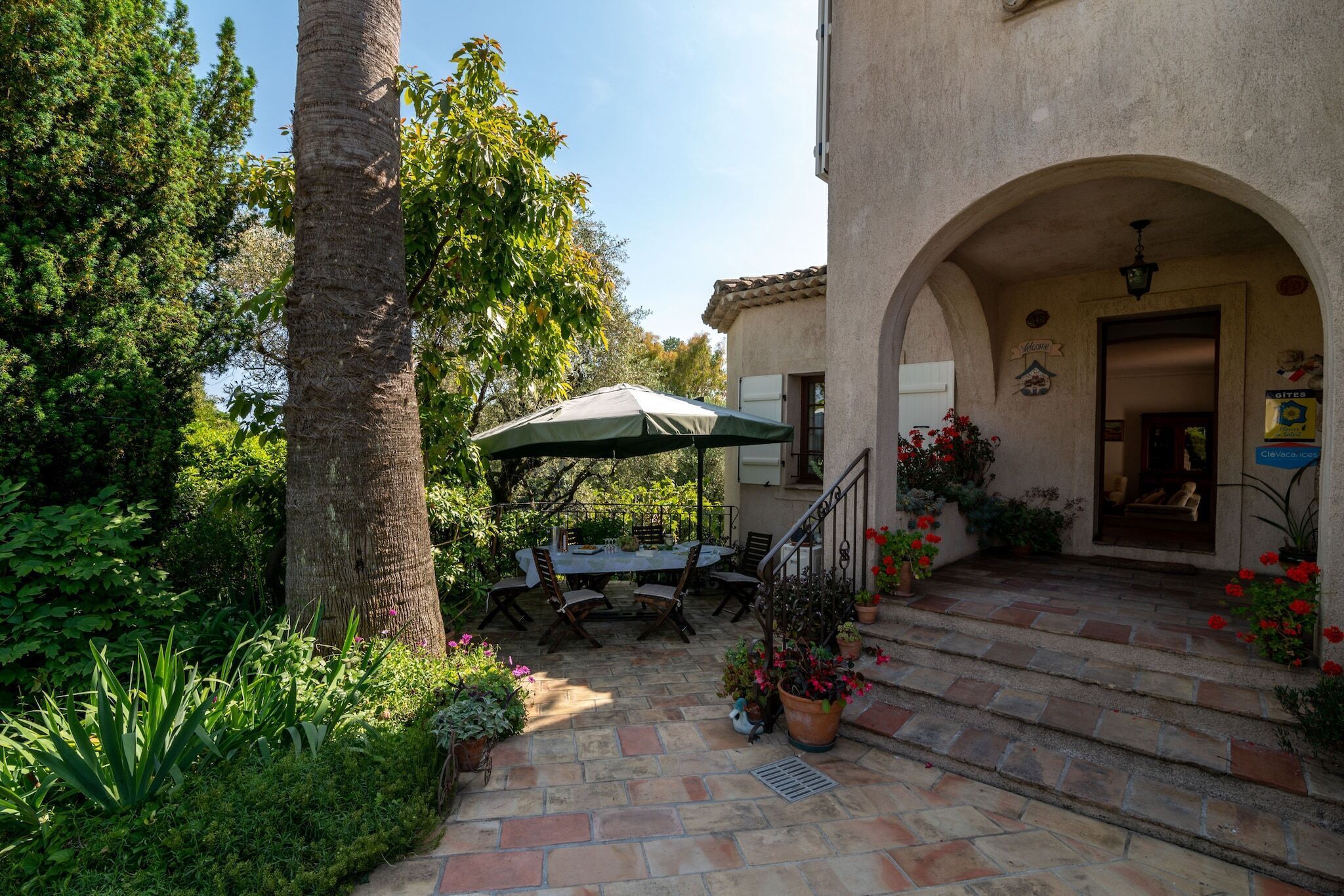 A patio with a table and chairs, an umbrella, and potted plants.