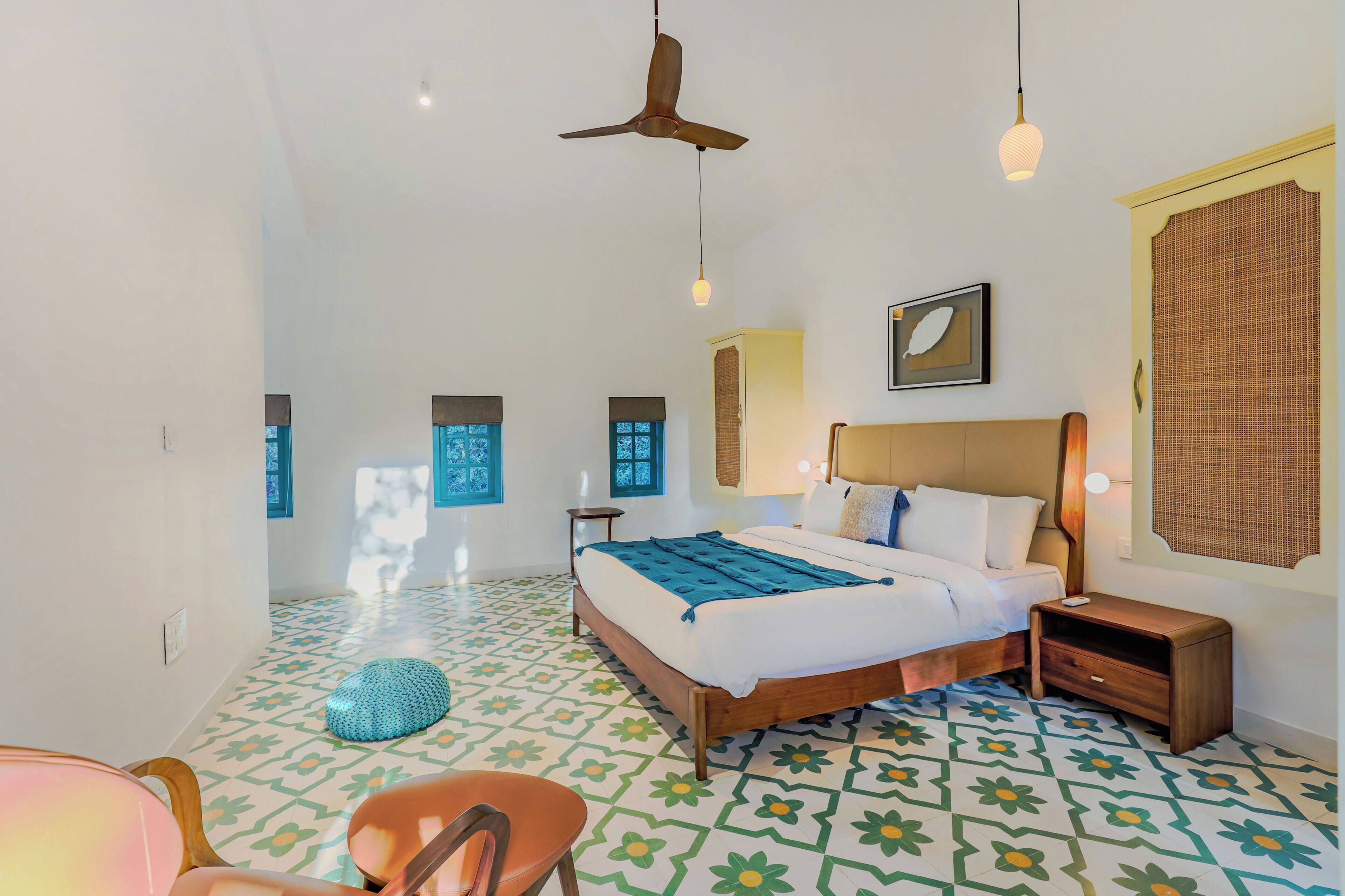 A bedroom with a bed, bedside table, wall-mounted lamp, ceiling fan, and patterned floor tiles.