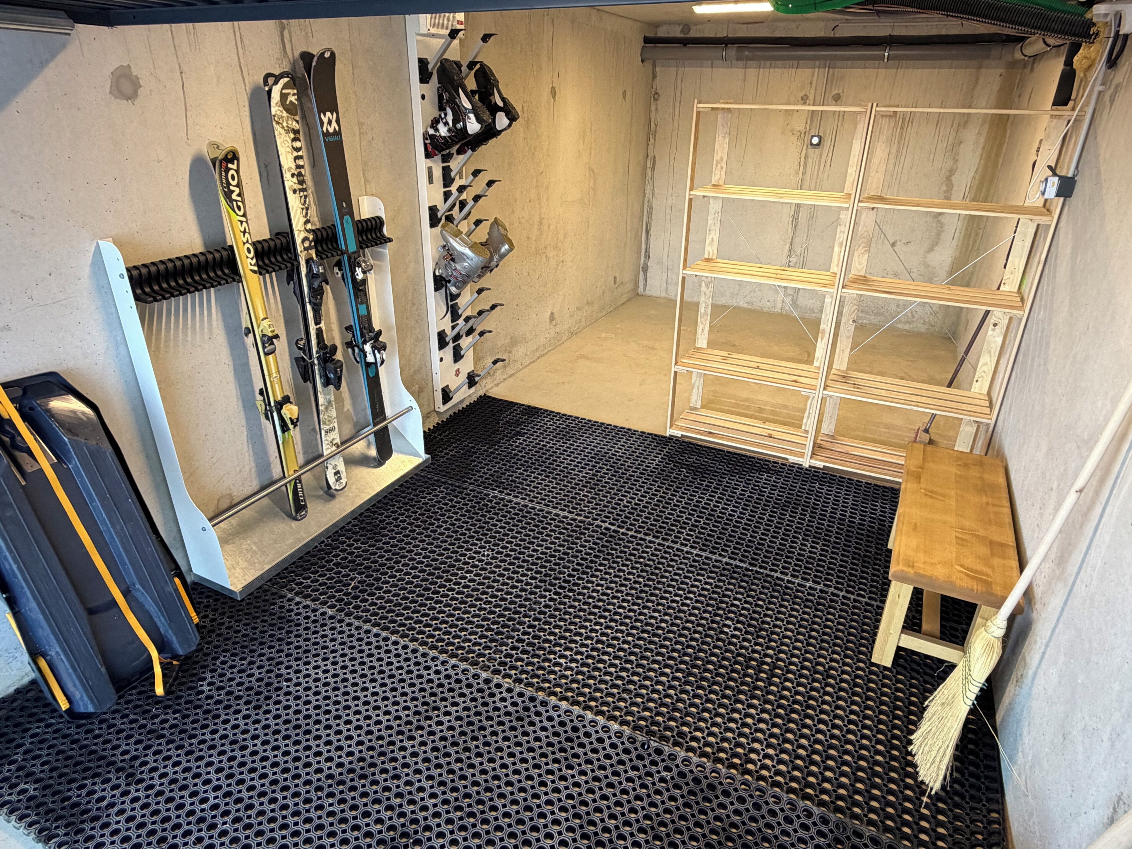 Zona d'emmagatzematge d'esqui amb prestatges per a esquís i snowboards, una banca de fusta i un sòl de reixeta metàl·lica.