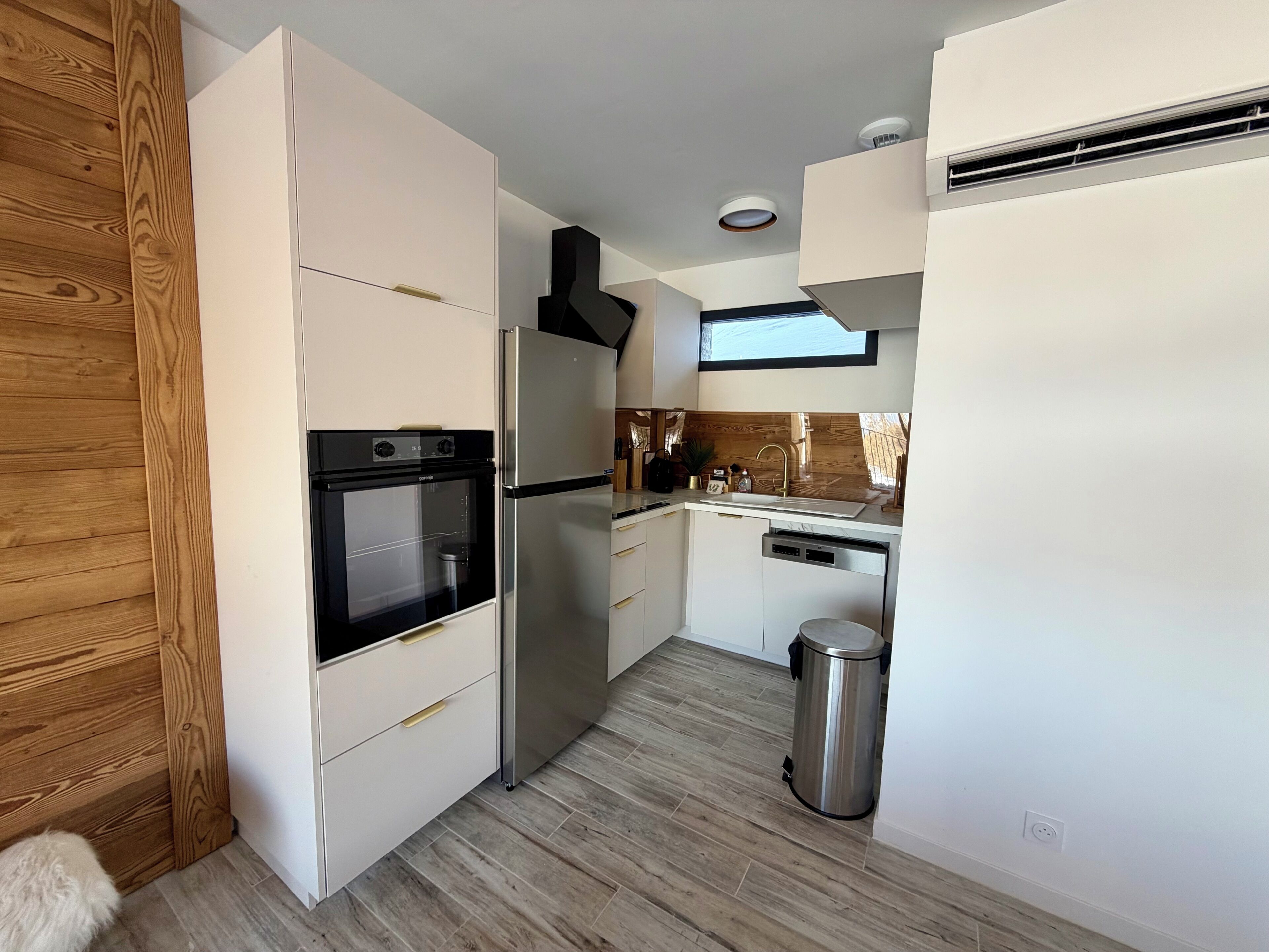 A compact kitchen with white cabinetry, a stainless steel refrigerator, a built-in oven, and a dishwasher.