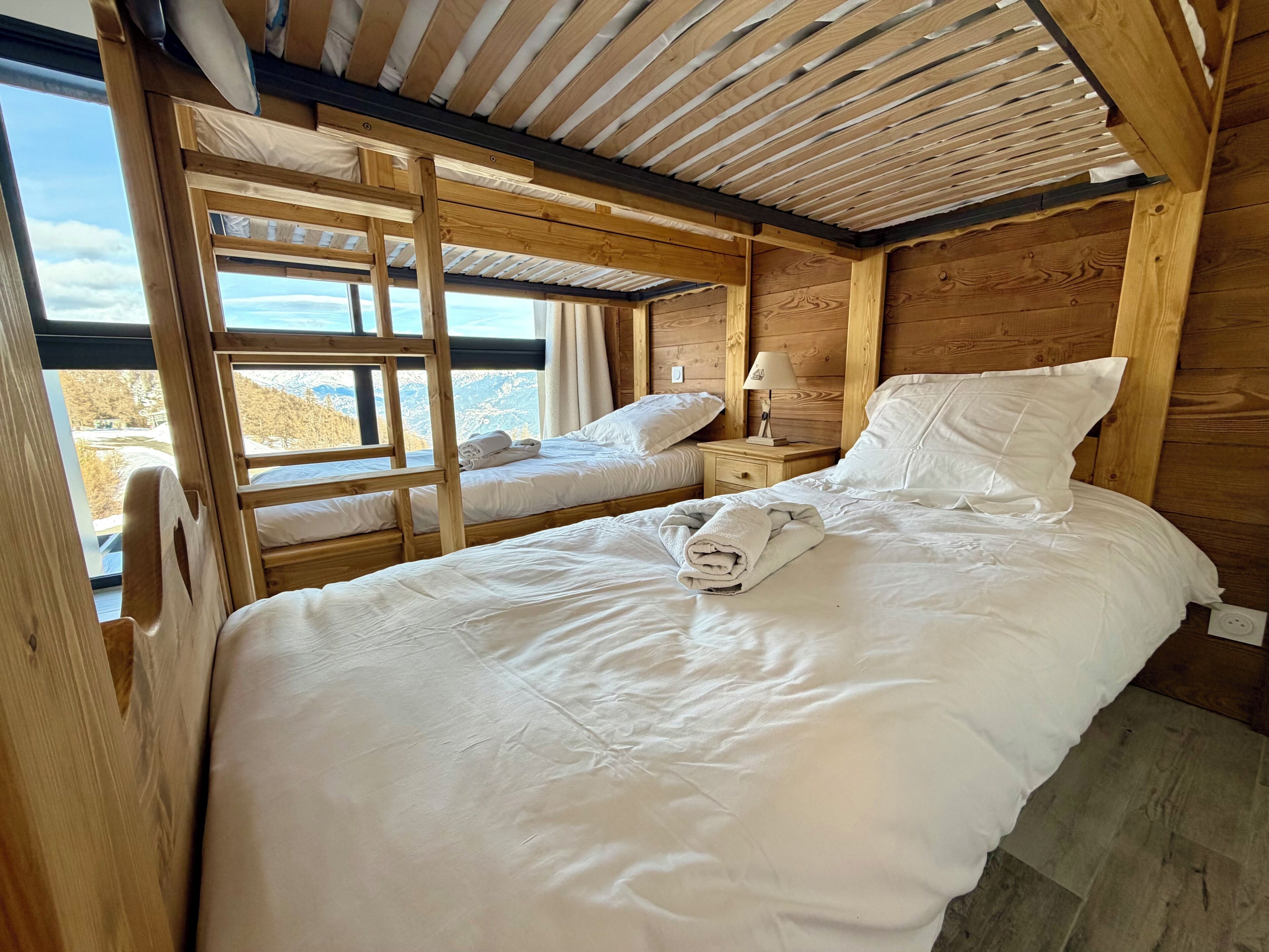 A wooden cabin bedroom with bunk beds, a nightstand, and a view of the outdoors.