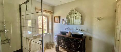 A bathroom with a glass shower enclosure, a wooden vanity with two sinks, and a large mirror above the vanity.