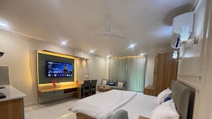 Ein modernes Hotelzimmer mit einem großen Bett, einem Schreibtisch mit Flachbildfernseher, einer Sitzecke mit Sofa und einem Kleiderschrank.