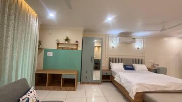 Una habitación de hotel moderna con cama, sofá, pequeño banco de madera, espejo y ventilador de techo.