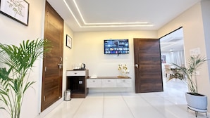 Eine moderne Hotellobby mit einem sauberen, gefliesten Boden, Holztüren, einem an der Wand montierten Fernseher und Topfpflanzen.