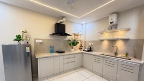 Eine moderne Küche mit einem Edelstahlkühlschrank, einer schwarzen Dunstabzugshaube, einem Spülbecken mit Armatur und einer Arbeitsplatte mit verschiedenen Gegenständen.