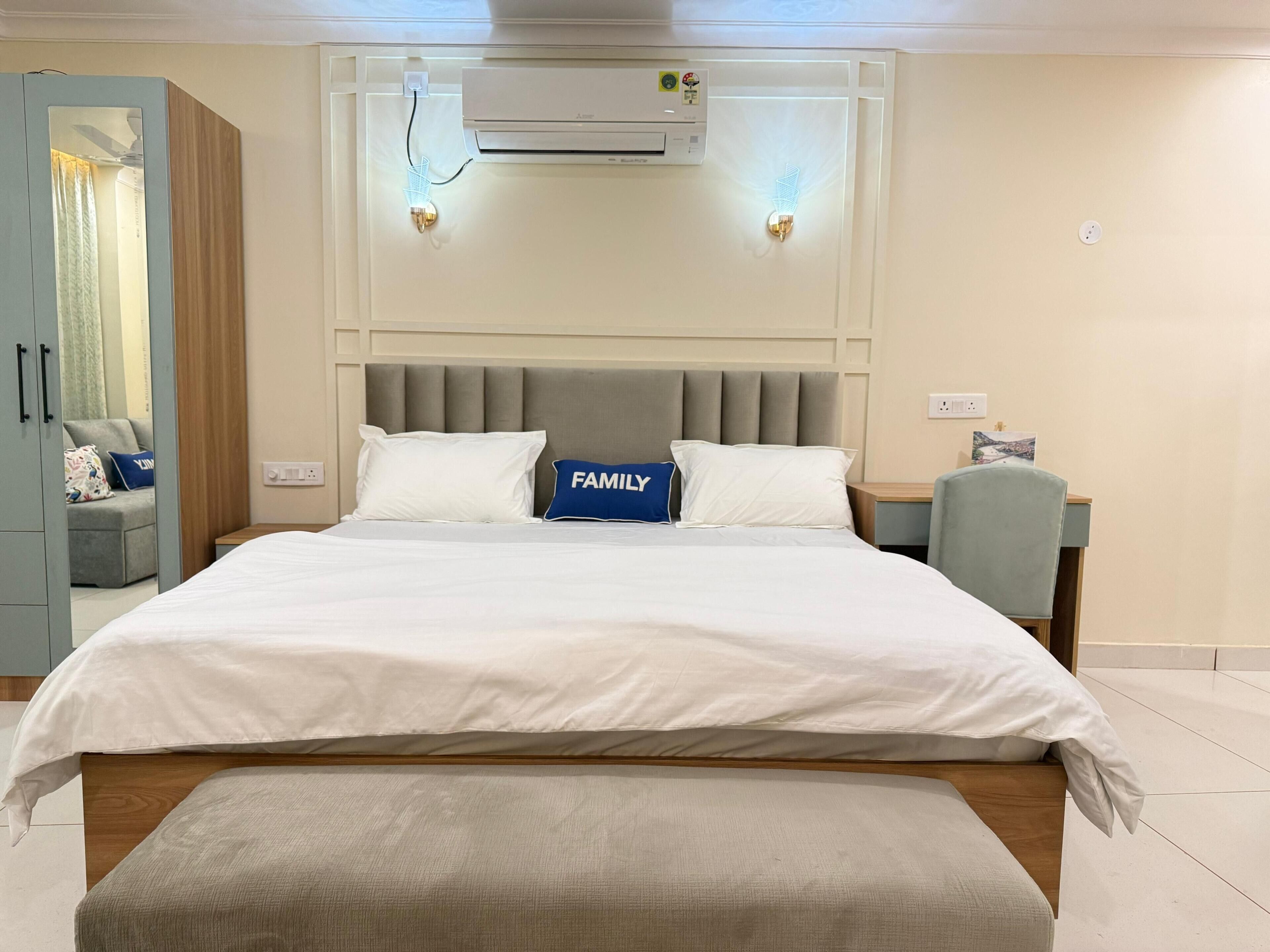 A hotel room with a bed, a bench, a wardrobe, and an air conditioning unit.