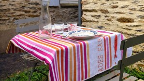 Ein Tisch im Freien mit gestreifter Tischdecke, einer Flasche, Gläsern und Tellern.